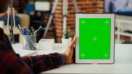 Office worker vertically holding digital device with greenscreen and isolated mockup template. Working with blank chroma key display with copy space background on wireless tablet. Close up.