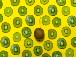 Background of many kiwi slices. One whole in the peel. Sliced kiwi on a yellow background. Raw food concept.   Pattern of green ripe fruit