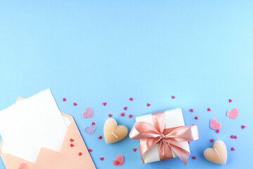Happy Valentine's Day greeting card template. Flat lay composition with romantic letter, gift box, heart-shaped candles, confetti on pastel blue table. View from above.