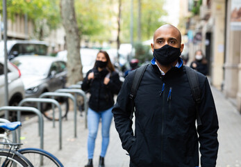 Portrait of young adult man wearing face mask for disease protection walking outside at cold day