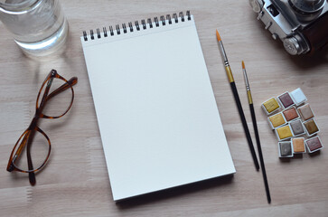 Espacio de trabajo/escritorio con bloc de papel para acuarelas/notas abierto en blanco, pinceles,...
