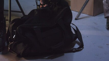 Robber in leather jacket taking black duffle bag and changing gloves in a dark basement