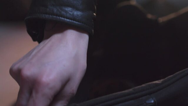 Close up of hands opening zipper of bag and pulls on leather gloves in basement