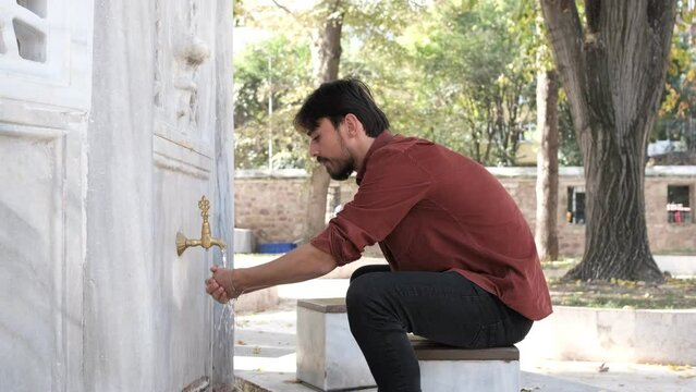 Side view of Muslim bearded man performing ablution, a man washing his mouth in mosque fountain, cleanliness is half of faith