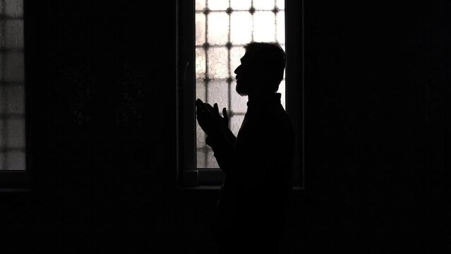 Image of a muslim silhouette young man sitting in front of a window praying in the mosque, people who believe in Islam worship