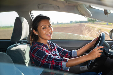 Positive hispanic woman driver sitting in car, side view