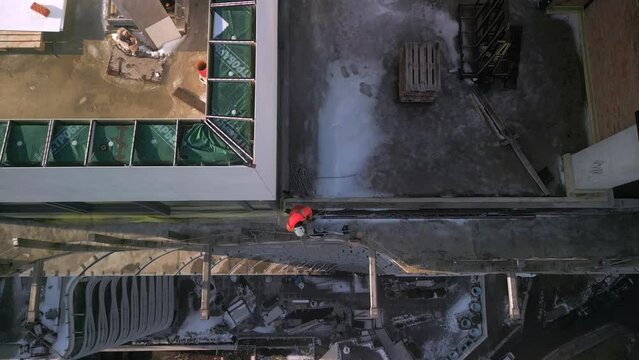 Aerial top down view of industrial climber in orange uniform drops a rope from a roof of modern high building