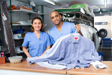 Positive man and woman workers of dry-cleaning facility posing at workplace