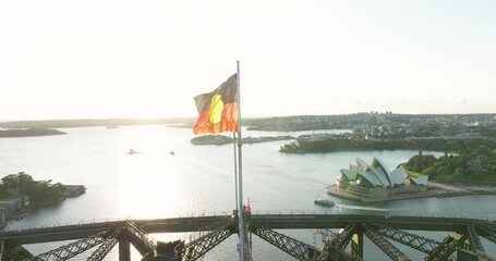 Australian Aboriginal Flag And Australian Blue Ensign Waving On Top Of Sydney Harbour Bridge At Sunrise In New South Wales, Australia. - aerial - Powered by Adobe