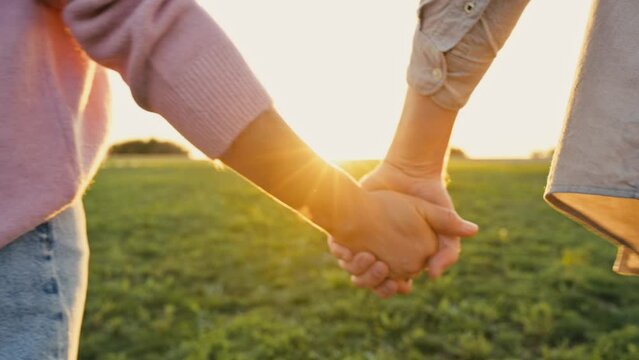 Close-up video of the hands of a man and a woman caucasian nationality tenderly holding each other while walking outdoors at sunset. Tenderness and romantic feelings