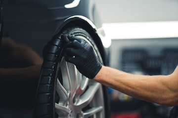 Close-up shot of unrecognisable man wearing black glove blackening tires of car using sponge....