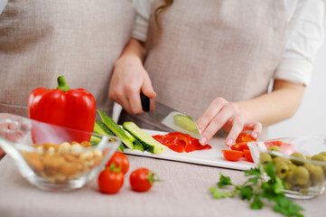 Close up cropped image of cutting board and couple cutting vegetables in the kitchen together, preparing food meal at home. Vegetarian healthy food Couple preparing a meal cut bell pepper