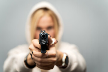 A girl in a hood is aiming a gun, front view, the main focus is on the barrel of the weapon, soft focus photo.
