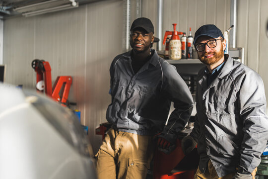 Medium shot of black and white mechanics posing for a picture and smiling. Repair shop concept. High quality photo