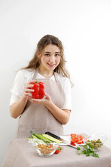 Smiling brunette woman holding red bell pepper while standing with hand on hip Green vegan salad with mixed green leaves Green salad with tomatoes and fresh vegetables