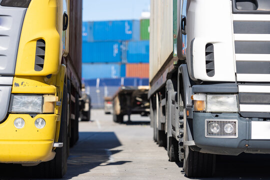 Trucks Standing On The Parking Lot By The Seaport With Colored Cargo Containers On The Background