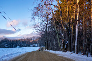 vintage suv drives away on snowy dirt road at sunset