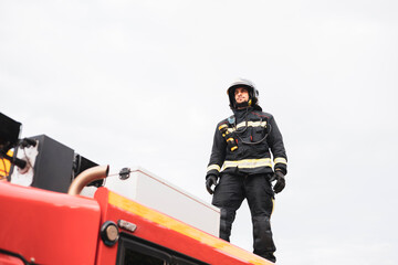 Fototapeta na wymiar A young uniformed firefighter climbs on top of a fire truck. Fire extinguishing service.