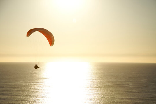 Paraglider rides the wind at sunset over the ocean in California.
