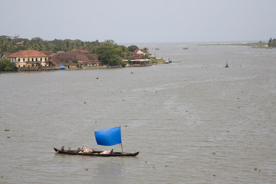 Small sailboat with blue tarp sail crosses waterway.