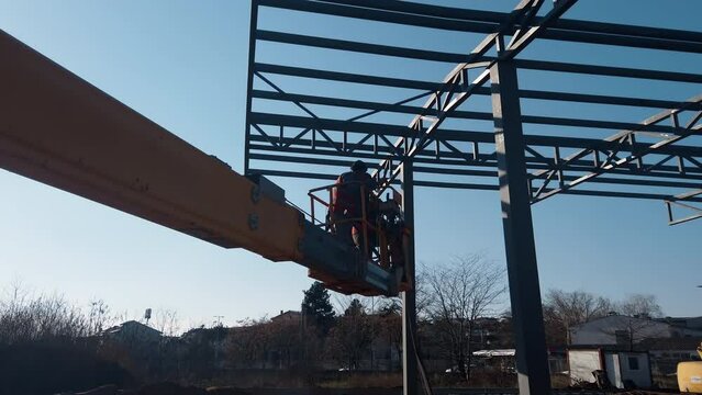 Cherry picker and crane beside metal frame of new building