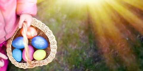 child collects colorful Easter eggs in basket. Easter egg hunt concept