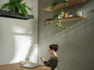 Young cheerful woman scroll on her phone sit by the desk
