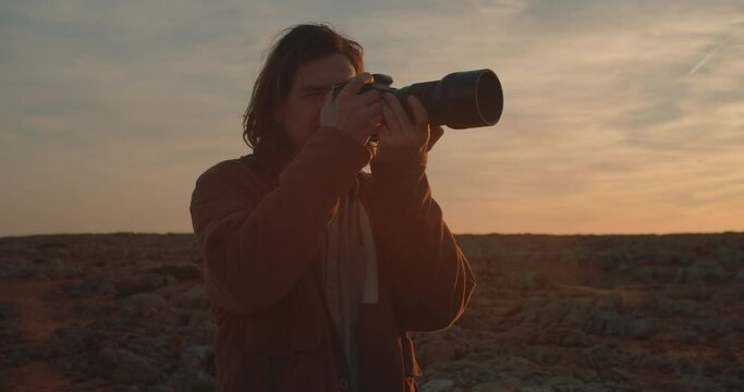 Long haired male photographer taking pictures and enjoying the scenery during sunset and blue hour on the coastline, cliffs of the Algarve, Portugal