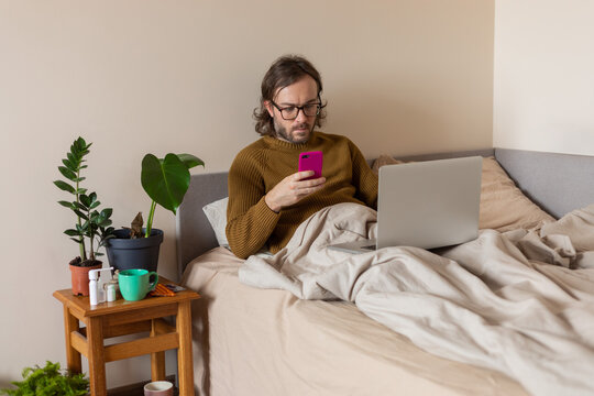 man in bed with laptop and phone