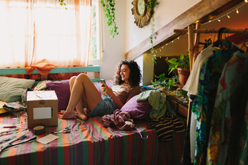 Woman typing on her phone sitting on her bed