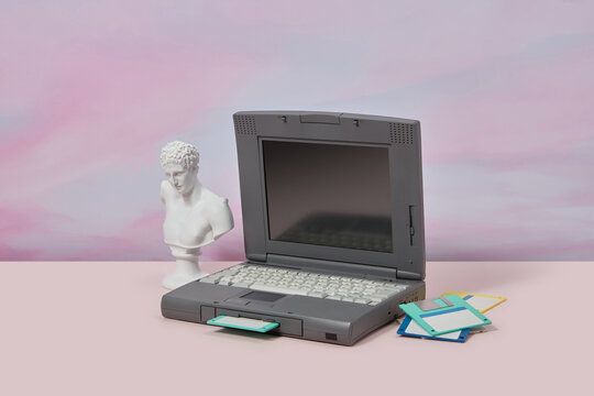 Old laptop with antique statue and floppy disks.