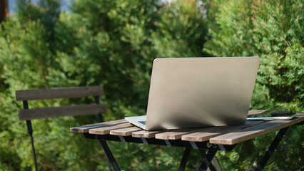 Fototapeta premium Laptop computer on wooden table with blurred nature view and sunlight in background
