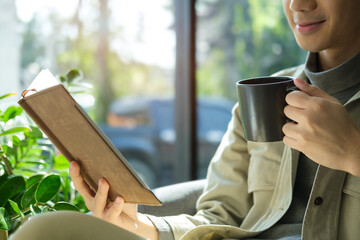 Cropped shot of young man reading a book and enjoying his coffee while sitting in cafe.