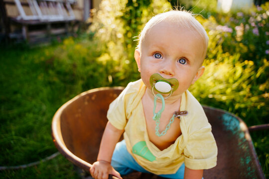 A child with a pacifier in his mouth is sitting in a cart