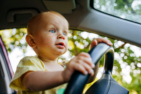 The child is sitting in the car at the wheel