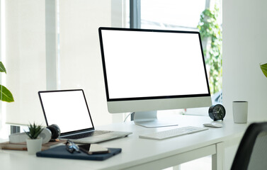 Modern workplace with blank screen computers, office supplies, headphone and books on white office desk.