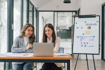 Two young pretty asia business woman in suit talking together in modern office workplace, Thai woman, southeast asian