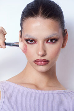 Androgynous woman With creative Make Up and a brush on her check