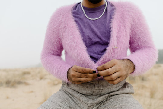 A man buttoning up the purple cardigan