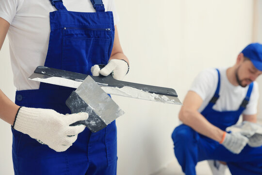 Professional workers with putty knives near wall indoors, closeup