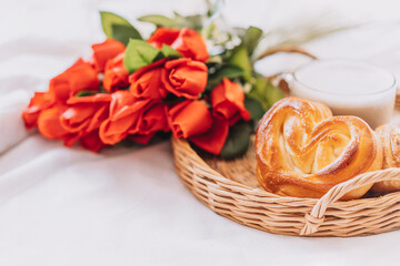 Wicker tray with pastries and coffee and flowers on white bed linen.