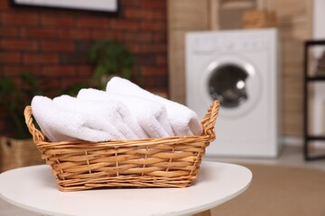 Fototapeta na wymiar Wicker basket with folded towels on white table in laundry room