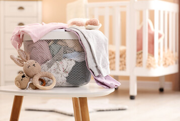 Laundry basket with baby clothes and crochet toys on white wooden table in child room, space for text