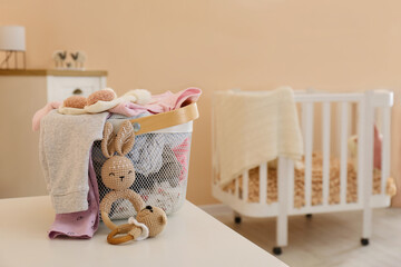 Laundry basket with baby clothes and crochet toys on white table in child room, space for text