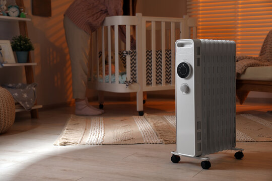 Woman near crib and modern portable electric heater indoors, closeup. Space for text