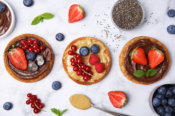 Tasty organic rusks with different toppings and ingredients on white marble table, flat lay