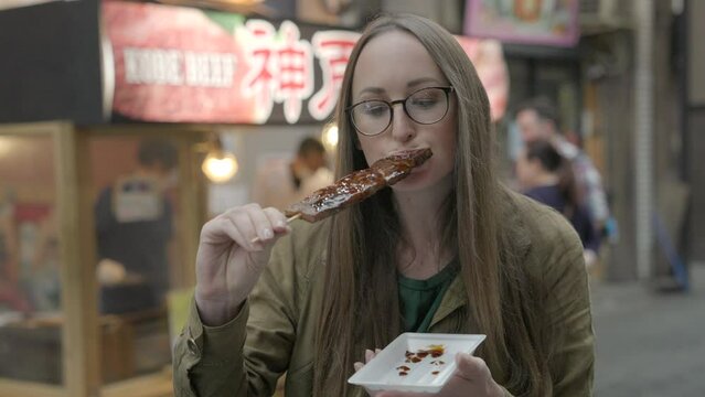 This video shows a woman eating glazes beef on a skewer in the streets of Japan.