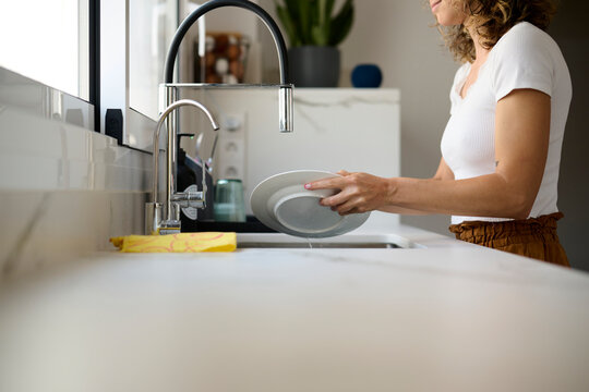 Woman washing plate in kitchen.