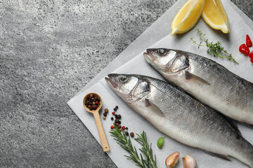 Sea bass fish and ingredients on grey table, above view. Space for text