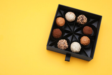 Box of tasty chocolate candies on yellow background, top view. Space for text